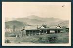 View of traditional built New Guinea building with mountain ranges in background, [Baiune?], New Guinea, c1929 to 1932