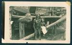 A man and child, sitting on beams in front of a building, New Ireland, New Guinea, [c1930?]